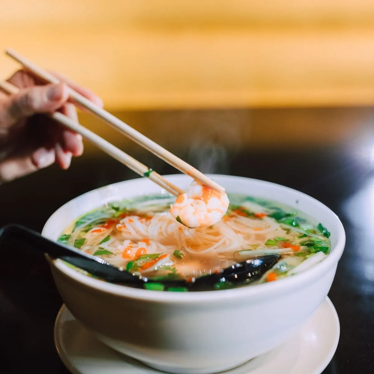 Sopa wantán con langostino, verduras y palitos apoyados en el tazón
